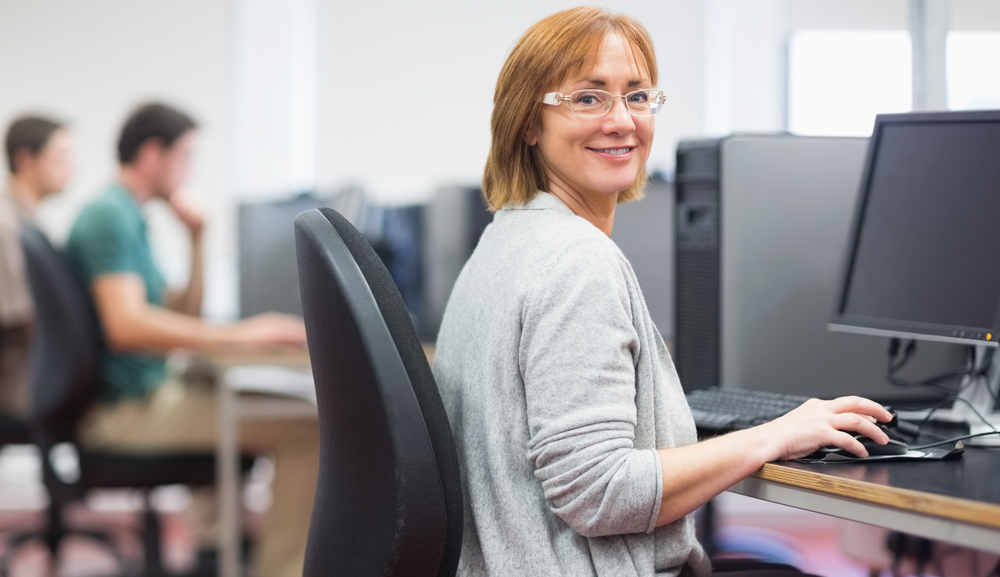 Portrait of a smiling woman by other mature students using computers in the computer room-1